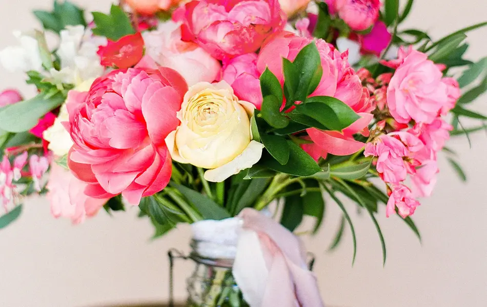 Peon- og rosebukett i glassvase med sløyfe på en pidestall