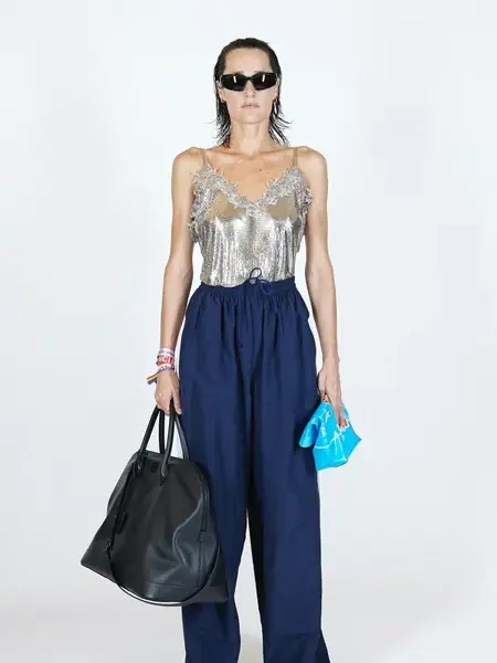 Dame med sølv topp og store vide mørkeblå joggebukse og en sort stor håndveske 