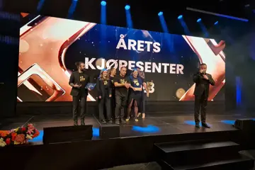 Ansatte på Kvadrat står samlet på stor scene etter å ha vunnet prisen, foran skjerm der det står årets kjøpesenter.