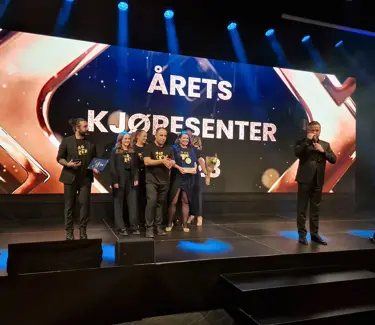 Ansatte på Kvadrat står samlet på stor scene etter å ha vunnet prisen, foran skjerm der det står årets kjøpesenter.