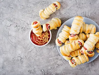 Scary sausage mummies in dough with funny eyes on table. Funny decoration. Halloween food. Top view. Flat lay