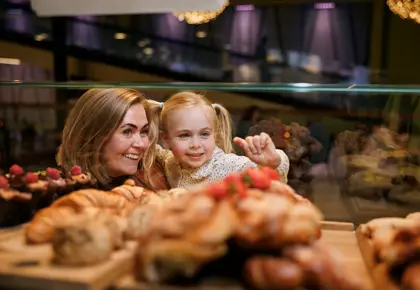 En kvinne og en liten jente står og ser inn gjennom glasset på bakverk som ligger der