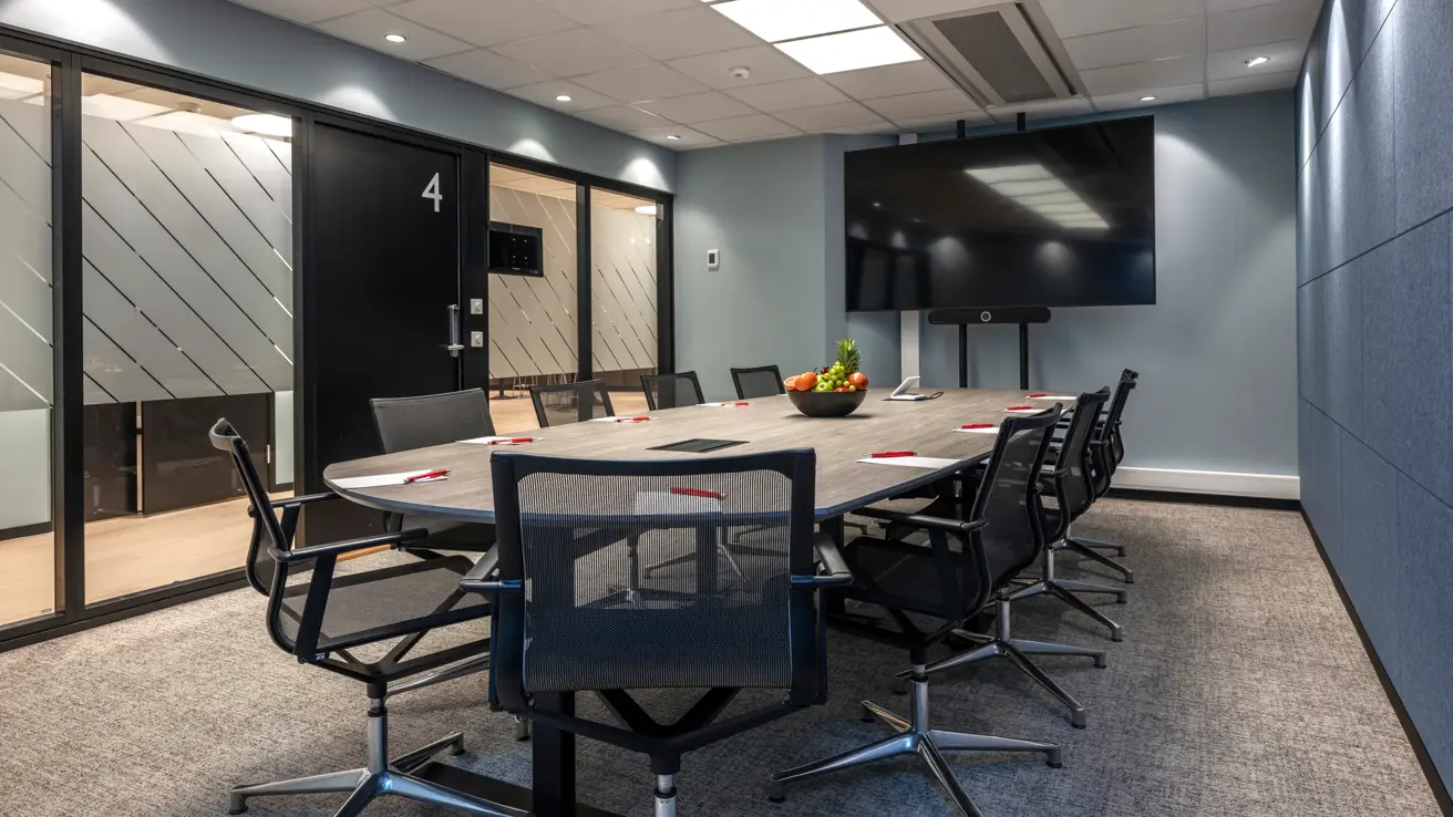 Møterom med styrebords oppsett til 10 personer. Stor skjerm, vegger i forskjellige blå farger og vinduer ut mot gang.