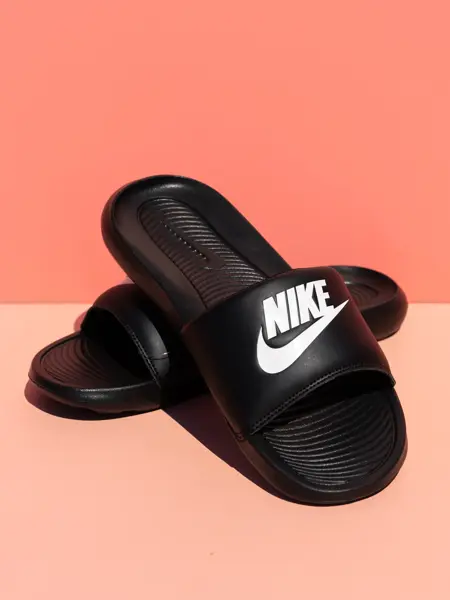Sorte Nike slippers på ferskenfarget bakgrunn