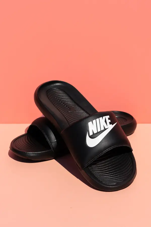Sorte Nike slippers på ferskenfarget bakgrunn