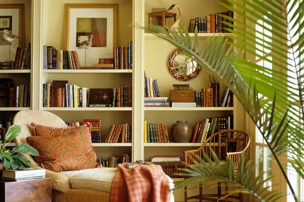 Divan med puter og pledd foran en bokhylle med bøker og pyntegjenstander