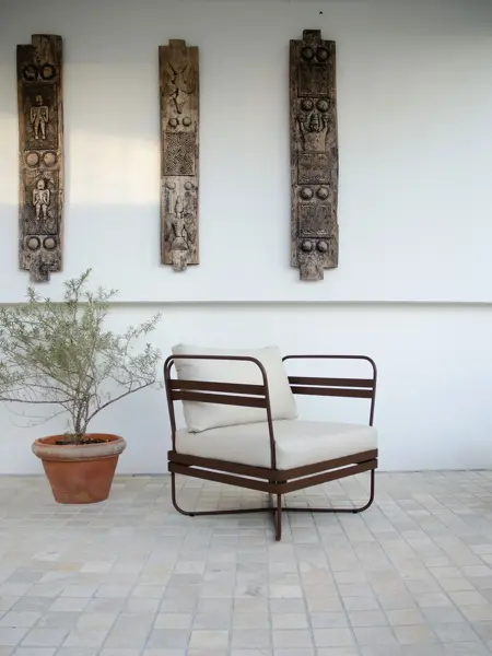 Brun stol med hvite puter og en grønn plante i terrakotta potte