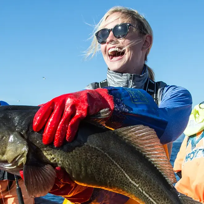 Fiskebåt, dame holder i en stor fisk. 