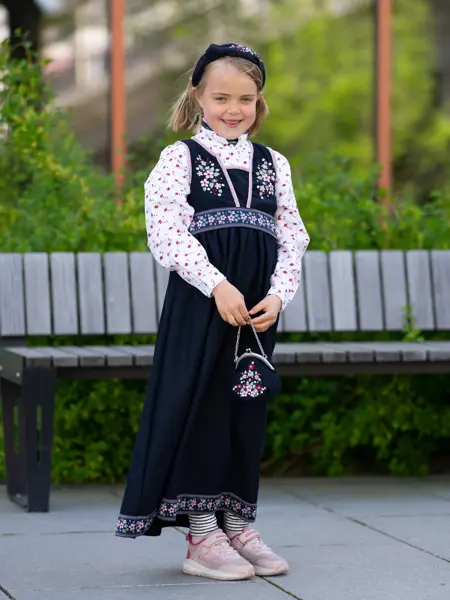 jente i mørk blå festdrakt, blomstrete kjole, hårbøyle og rosa sneakers.