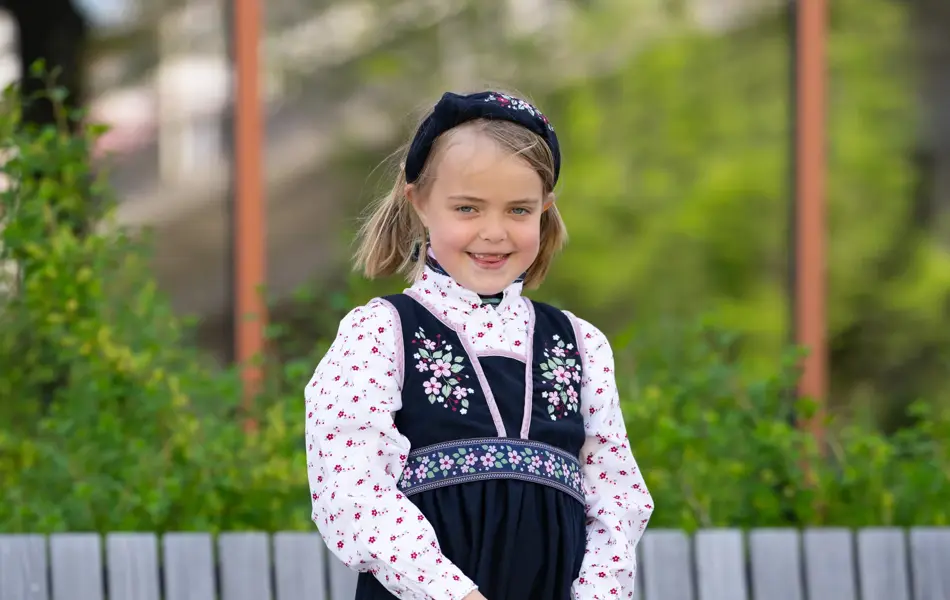 jente i mørk blå festdrakt, blomstrete kjole, hårbøyle og rosa sneakers.