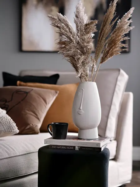 Hvit vase med strå og puter i bruntoner