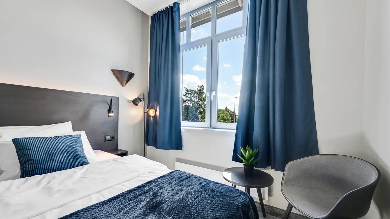 Enkeltseng, hvite vegger, vindu, blå gardiner, lenestol