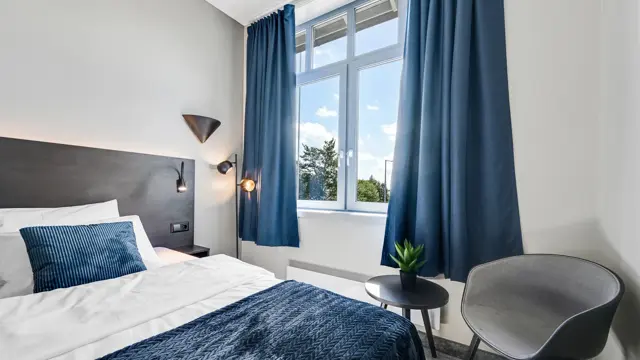 Enkeltseng, hvite vegger, vindu, blå gardiner, lenestol