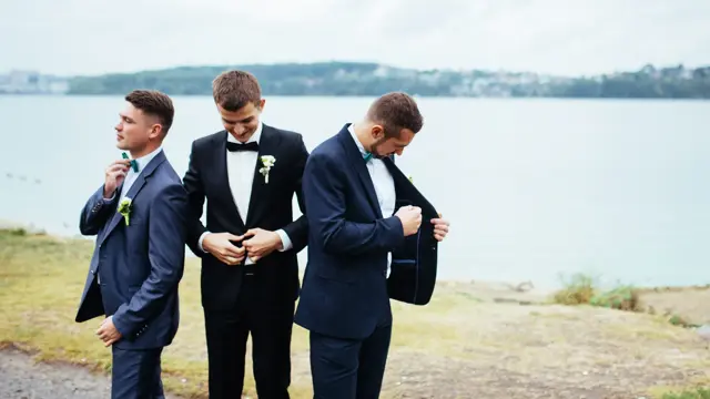 Confident smiling handsome groom in black suit with two groomsman