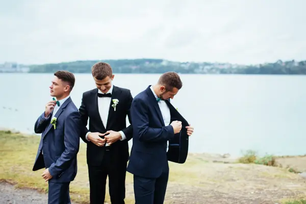 Confident smiling handsome groom in black suit with two groomsman