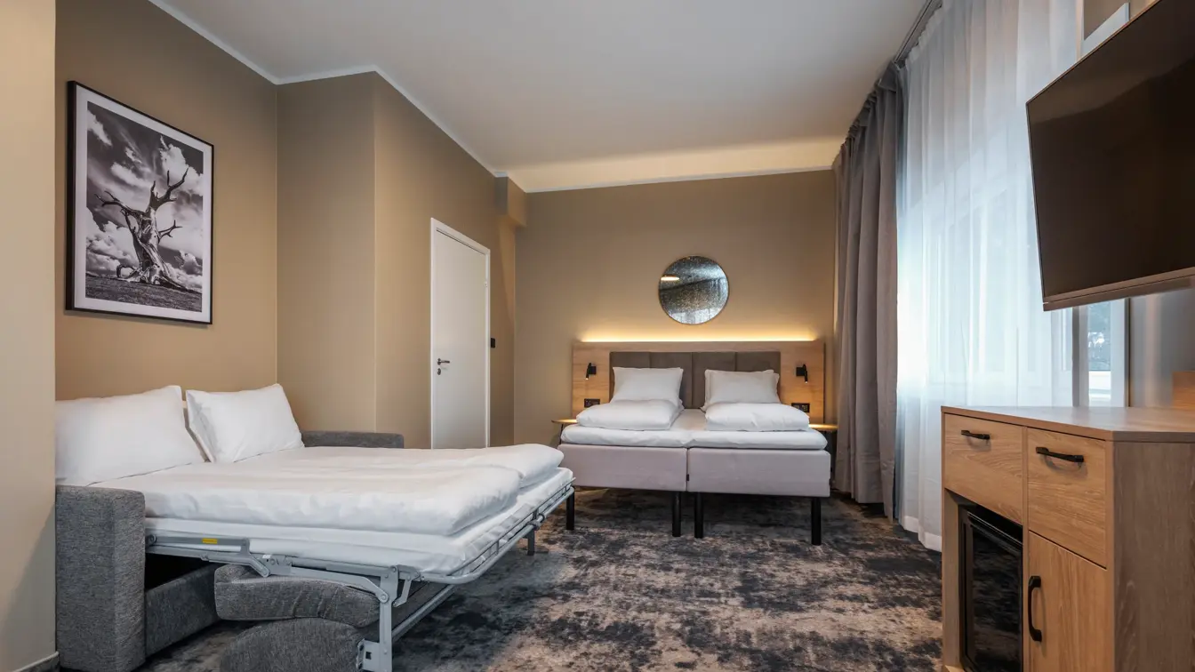 Junior suite med dobbeltseng og oppredd sovesofa, teppegulv, TV med TV benk under og minibar.