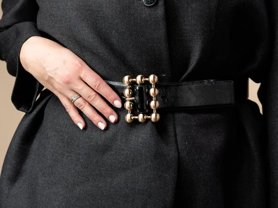 Vårens trender. Jente med halvlangt blondt hår inne i en butikk. Har på seg en trenchcoat, knall rosa kjole og en sort dressjakke med belter