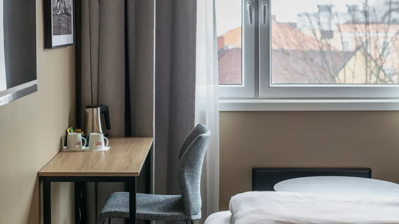 Utsnitt av dobbeltrom med twin senger, med skrivebord, stol, bilde og TV på veggen.