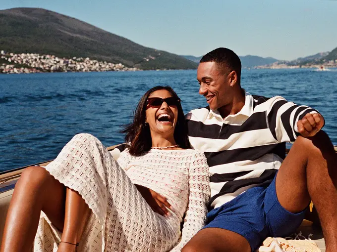 Par sitter foran på båt og smiler og ler i sola