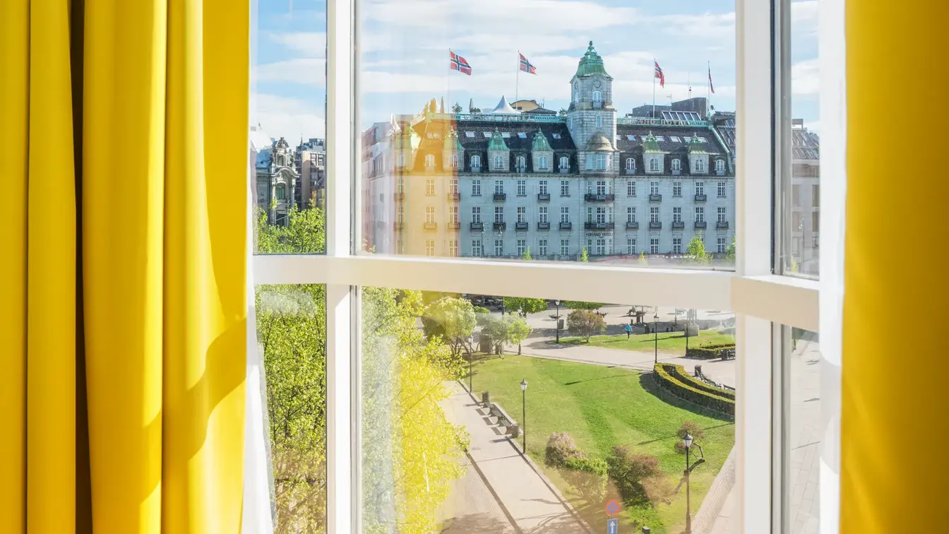 Gule gardiner og store vinduer med utsikt over Stortinget i junior suite på Thon Hotel Cecil