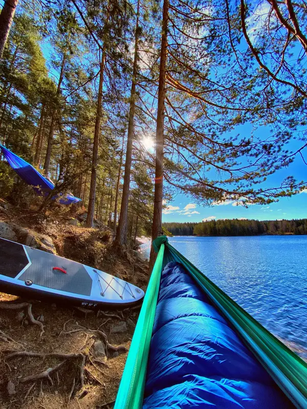 Utsnitt av tuppen på en hengekøye og et sup-brett i vannkanten