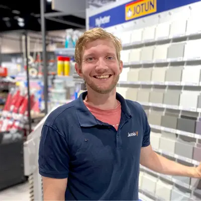 Mann ansatt som smiler ved siden av en vegg med fargeprøver