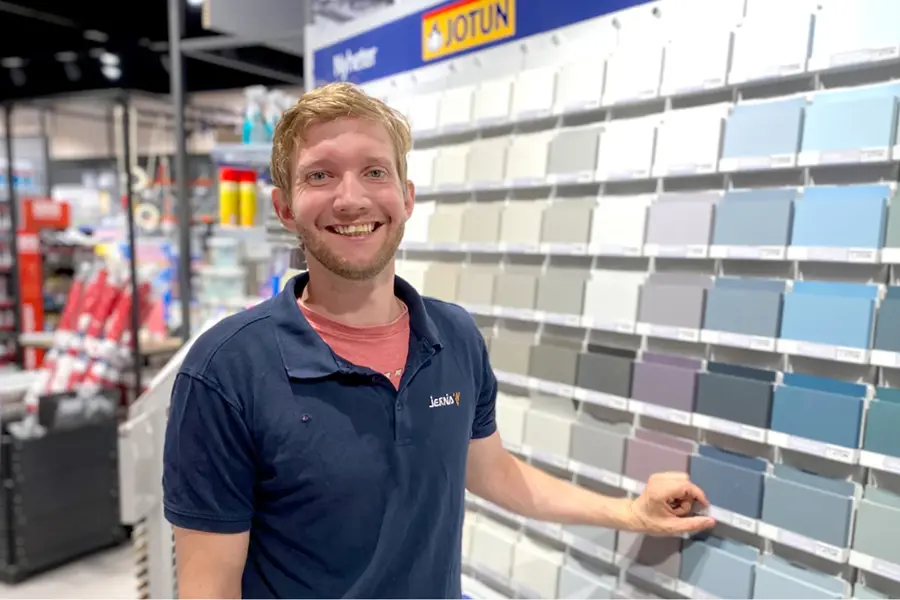 Mann ansatt som smiler ved siden av en vegg med fargeprøver