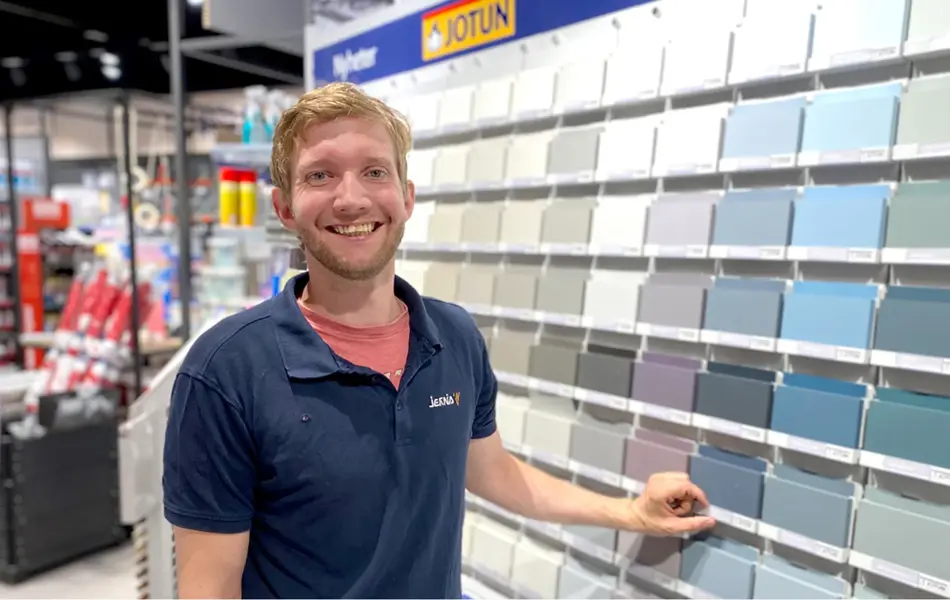 Mann ansatt som smiler ved siden av en vegg med fargeprøver