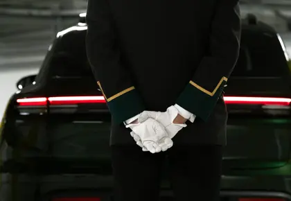 En ansatt står med hendene på ryggen, med ryggen til med en bil foran seg.