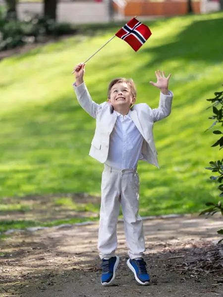 Liten gutt i hvit dress, hvit skjorte og blå sneakers.