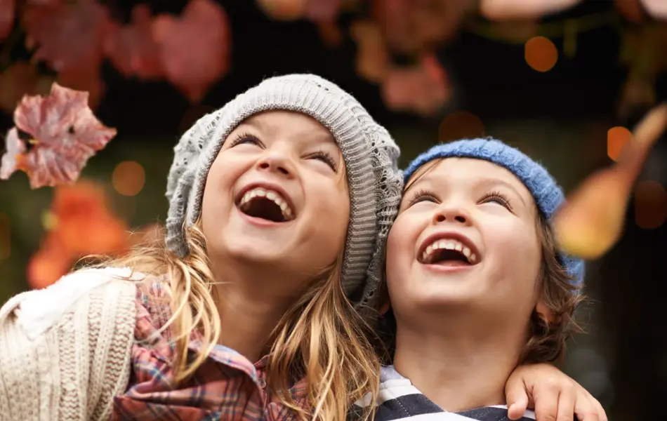 Shot of two cute kids laughing joyfully while watching autumn leaves falling from the trees