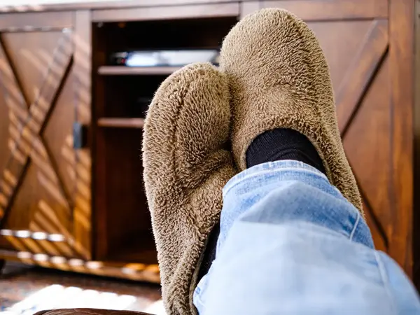 Førstepersonsperspektiv på bein med tøfler, ligger på sofa, skap i uskarp bakgrunn. Foto til artikkel om gaver til pappatyper på farsdag.