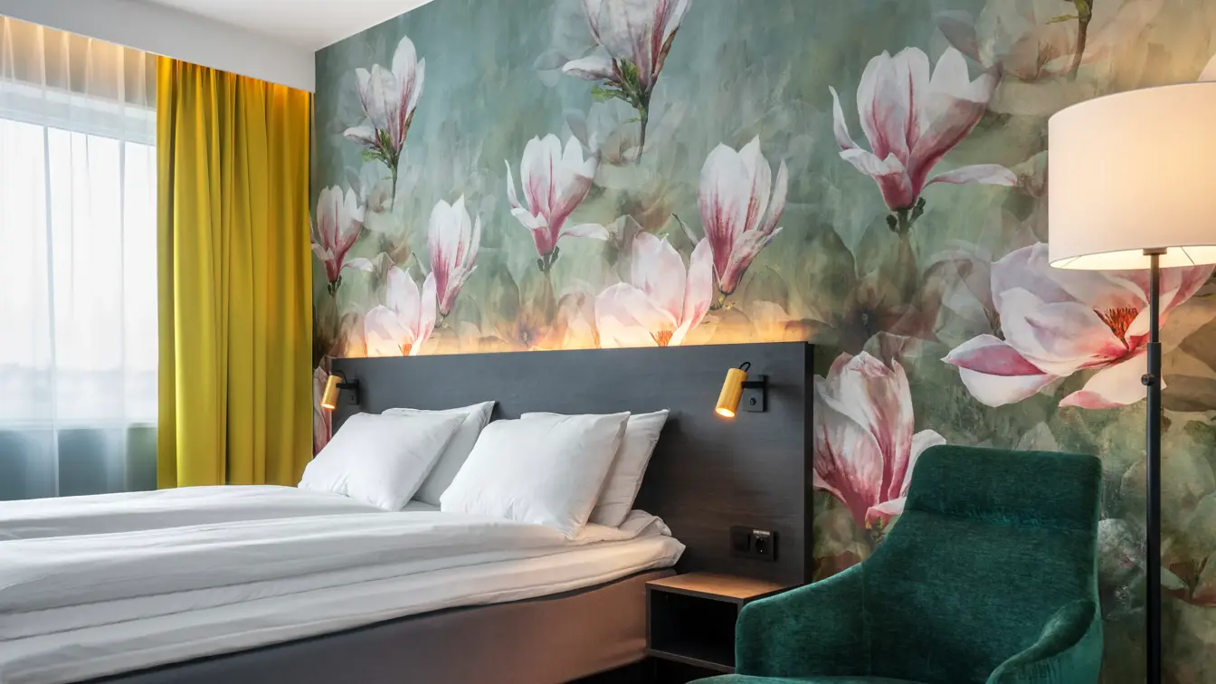 Blomstertapetvegg, dobbeltseng, grønn lenestol, gulvlampe, vindu, gule gardiner