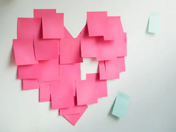 Blank pink sticky notes sticked in a heart shape on wall.