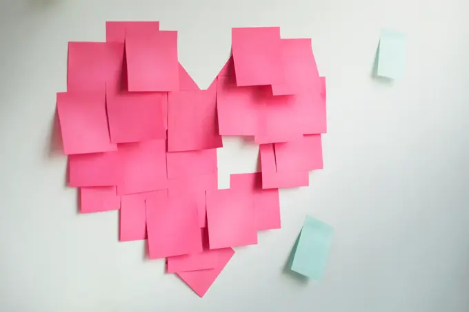 Blank pink sticky notes sticked in a heart shape on wall.