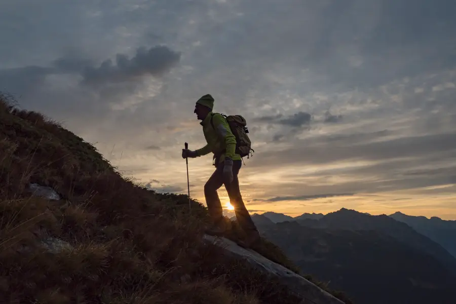 Mann går med stav i solnedgangen opp et fjell