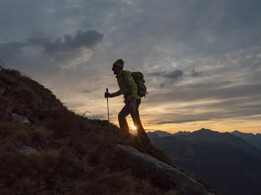 Mann går med stav i solnedgangen opp et fjell