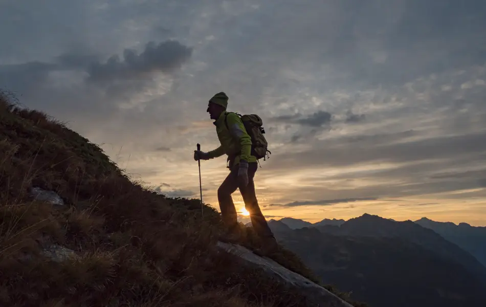 Mann går med stav i solnedgangen opp et fjell