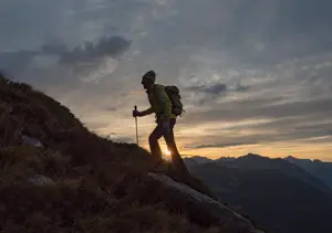 Mann går med stav i solnedgangen opp et fjell