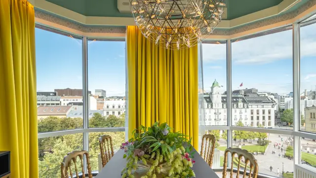 Spisestue i suite med store vinduer og utsikt. Lysekrone i taket og gule gardiner