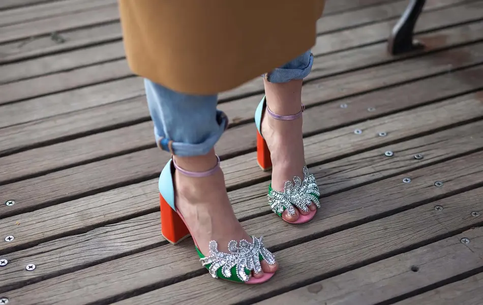 Nærbilde av et par dameføtter i høyhælte sandalpumps med glitter, strass, rød hæl og lyseblå detaljer. Illustrasjonsbilde til artikkel om vårmote for sko.