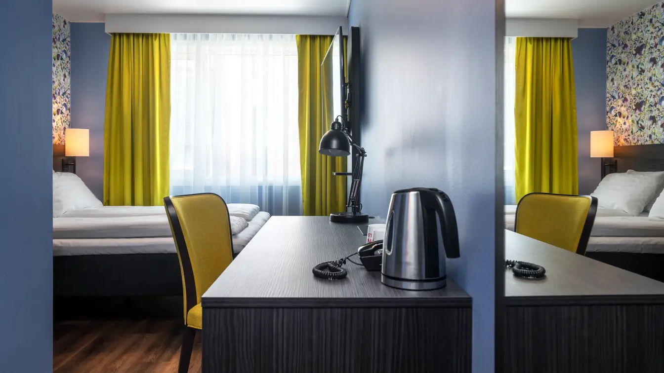 Tapetvegg, dobbeltseng, skrivebord, blå vegg, vindu, gule gardiner.