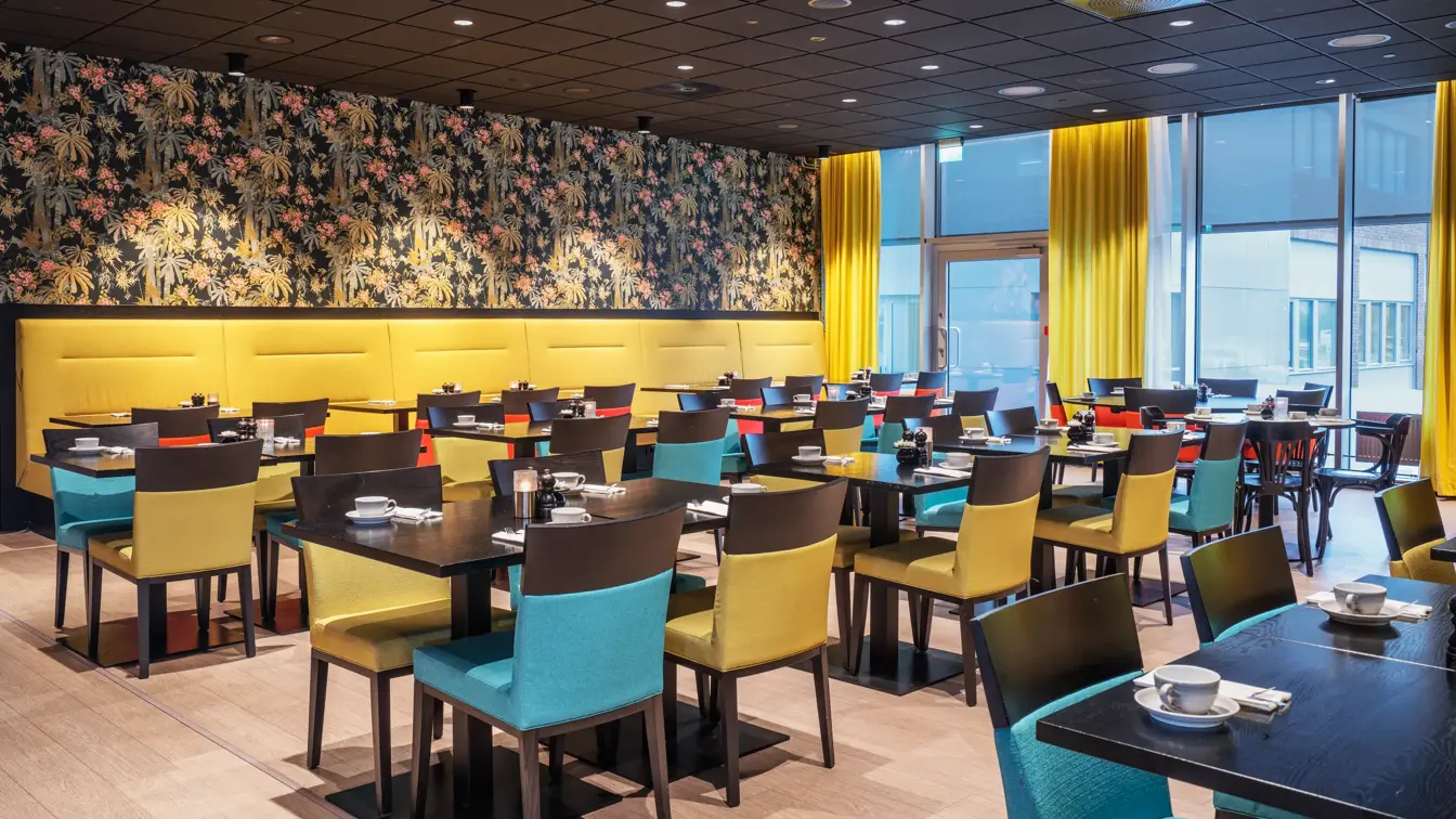 Tapetvegg med mønster, vindu fra gulv til tak, gule gardiner, spisebord med stoler, lys parkett. 