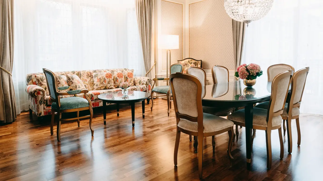 Blomstersofa, parkettgulv, spisebord, beige stoler, lysekrone, vindu, grønne stoler