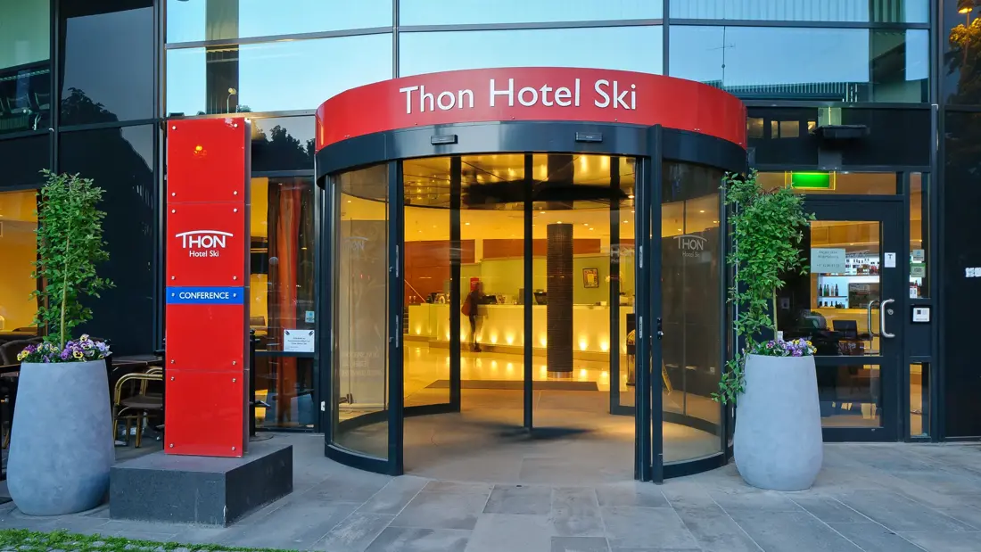 Inngangspartiet til Thon Hotel Ski med rødt skilt som viser hotellets navn og svingdør inn til lobbyen