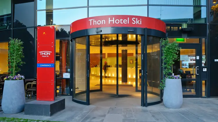 Inngangspartiet til Thon Hotel Ski med rødt skilt som viser hotellets navn og svingdør inn til lobbyen