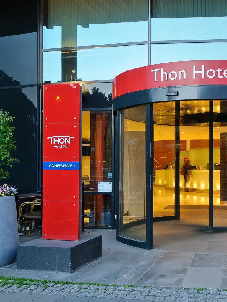 Inngangspartiet til Thon Hotel Ski med rødt skilt som viser hotellets navn og svingdør inn til lobbyen