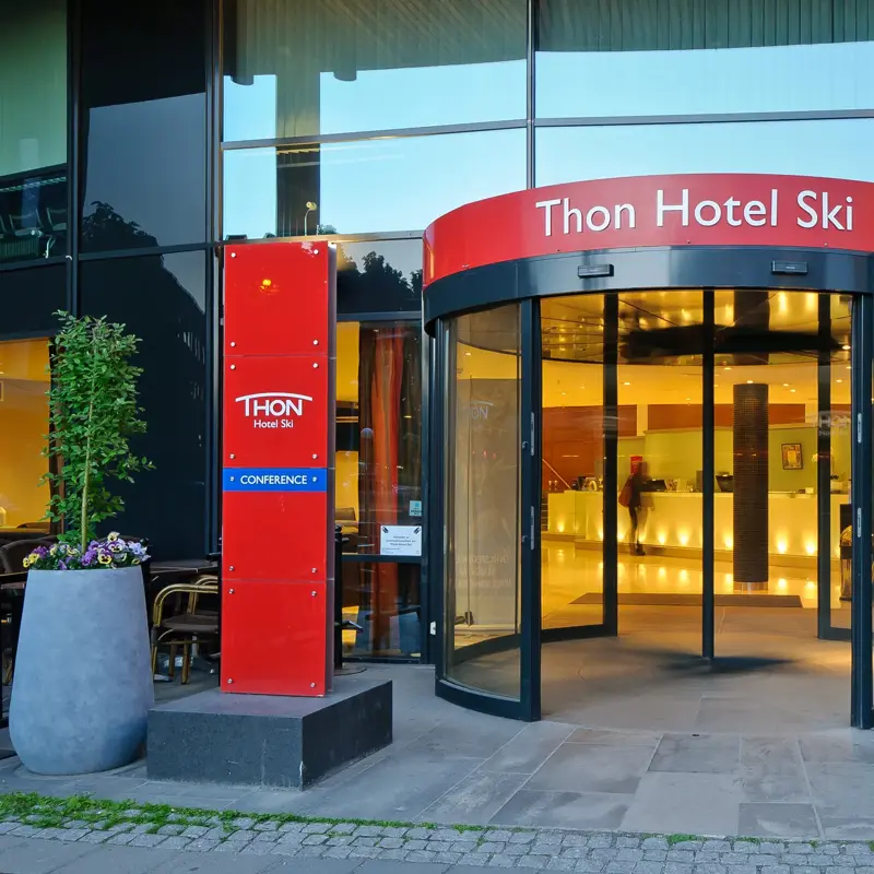 Inngangspartiet til Thon Hotel Ski med rødt skilt som viser hotellets navn og svingdør inn til lobbyen