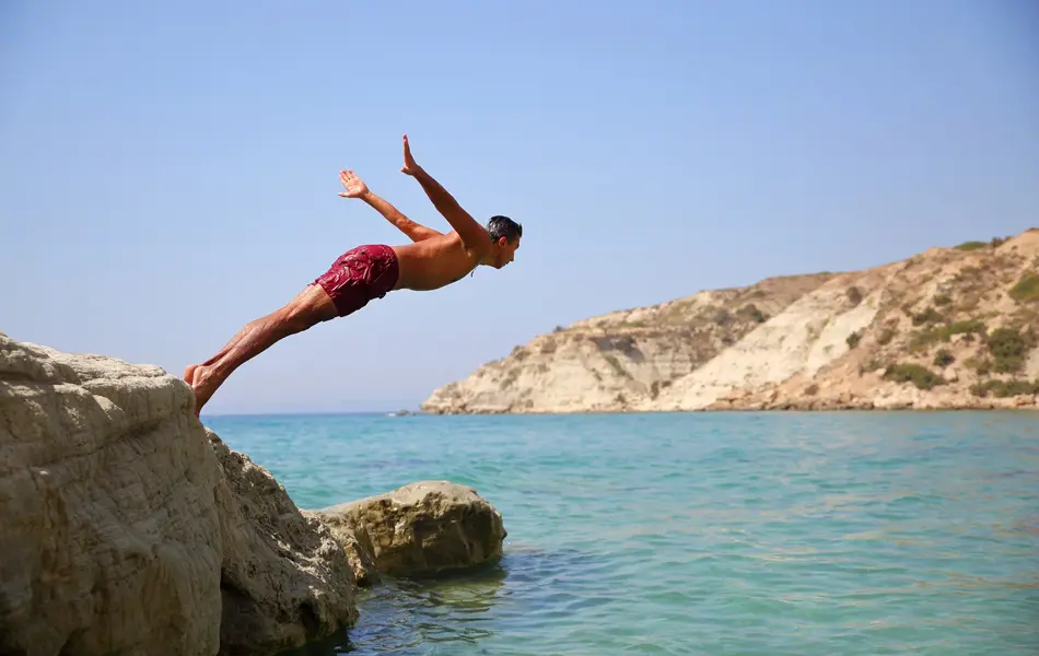 Mann i våt badebukse stuper fra en klippe.