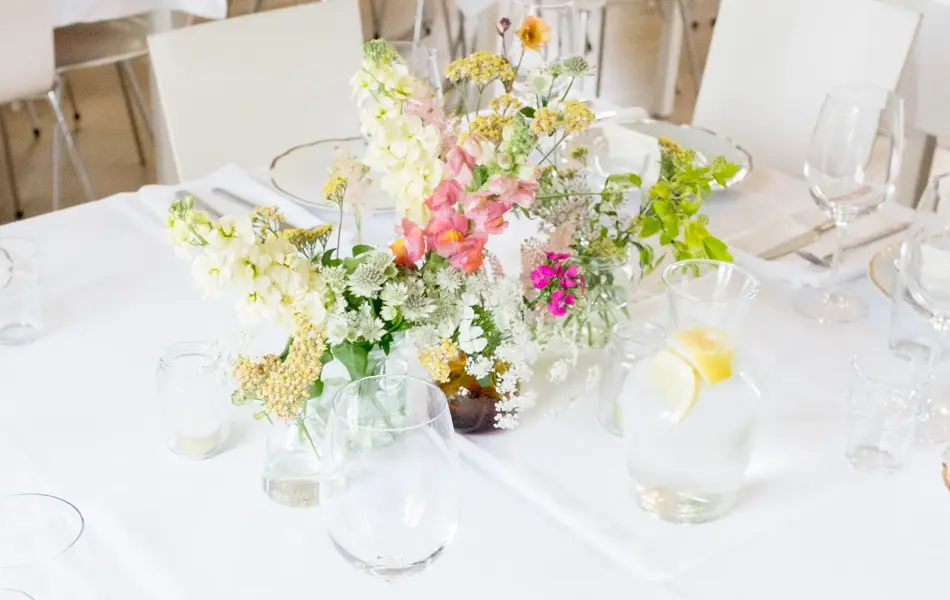 Hvitdekket bord dekorert med markblomster i små vaser